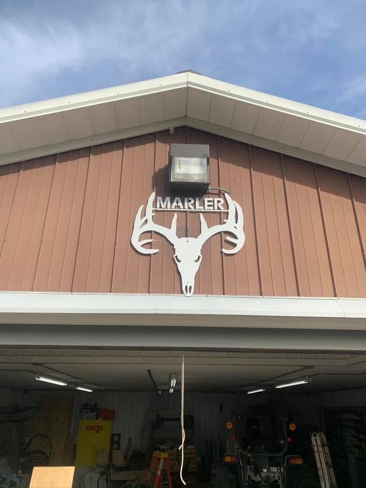 White CNC plasma-cut MARLER deer skull sign mounted on the front of the shop