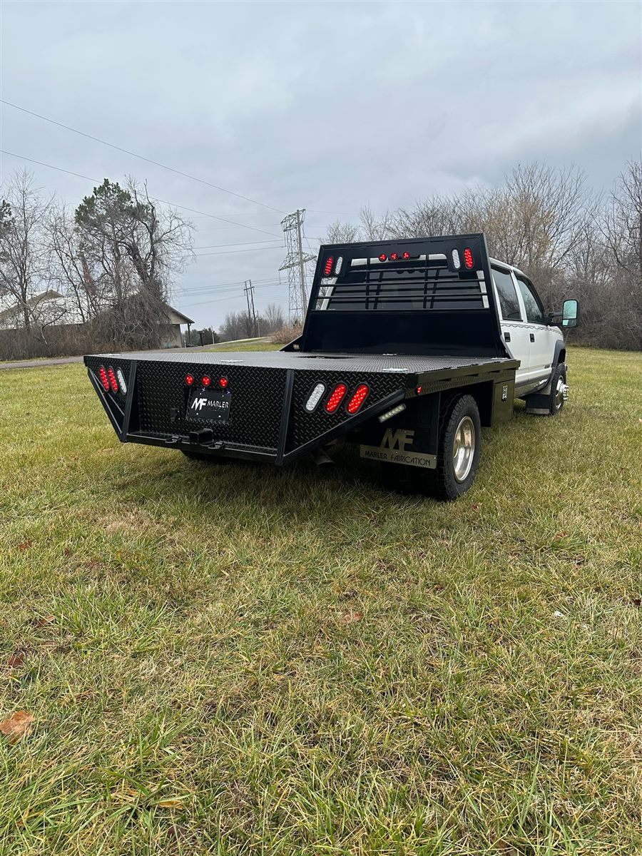 Flatbed on a white crew-cab dually, seen from the rear corner