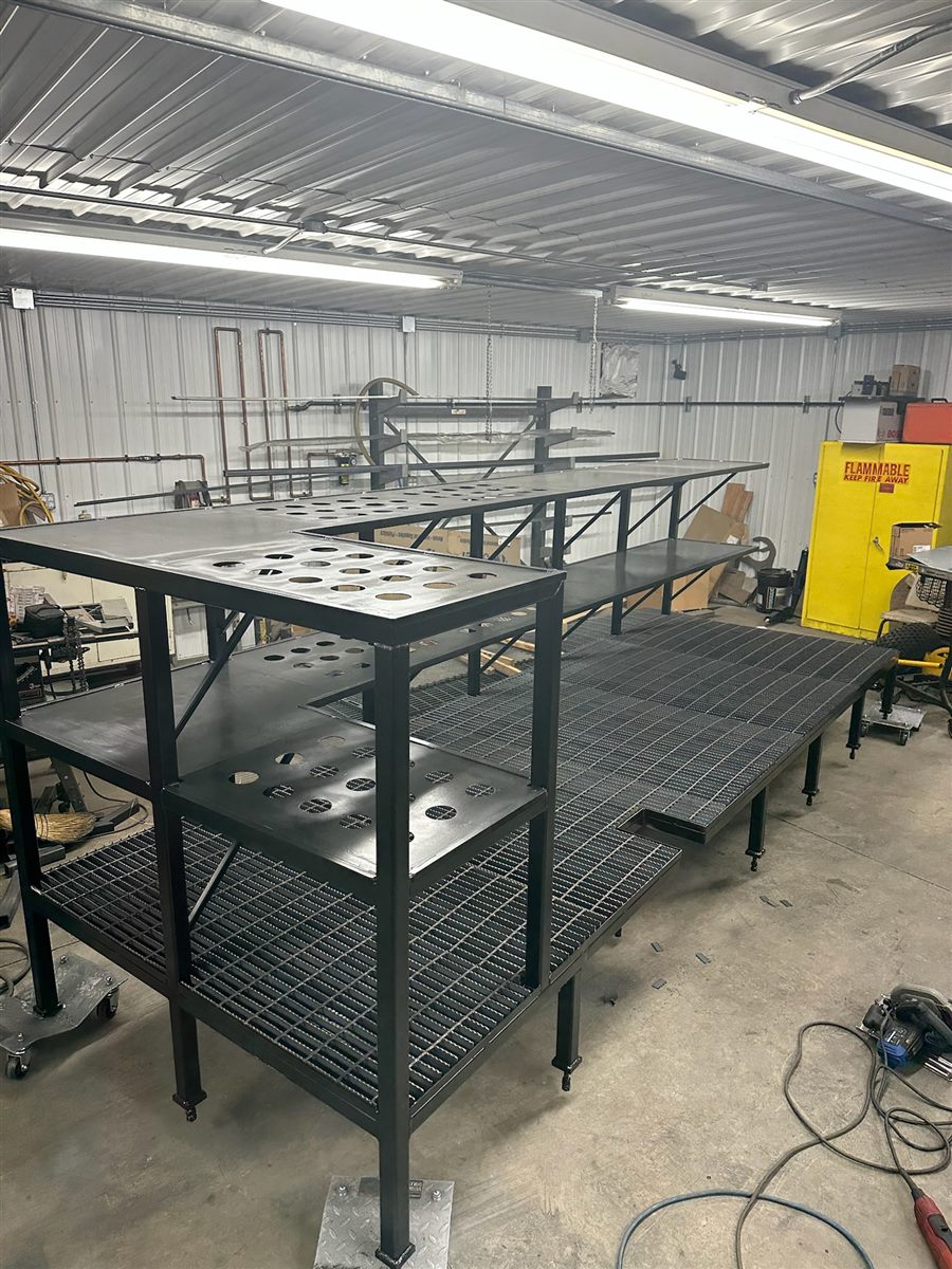 Long steel platform with grating decks and a tiered upper shelf, in the shop
