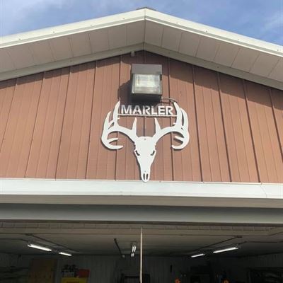 White CNC plasma-cut MARLER deer skull sign mounted on the front of the shop