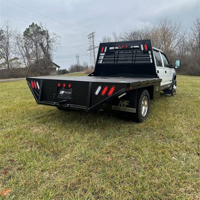 Flatbed on a white crew-cab dually, seen from the rear corner