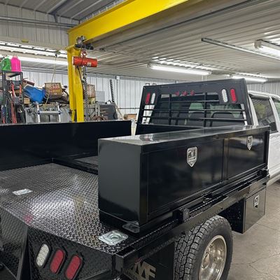 Black steel flatbed with top-mount toolboxes and a headache rack, in the shop